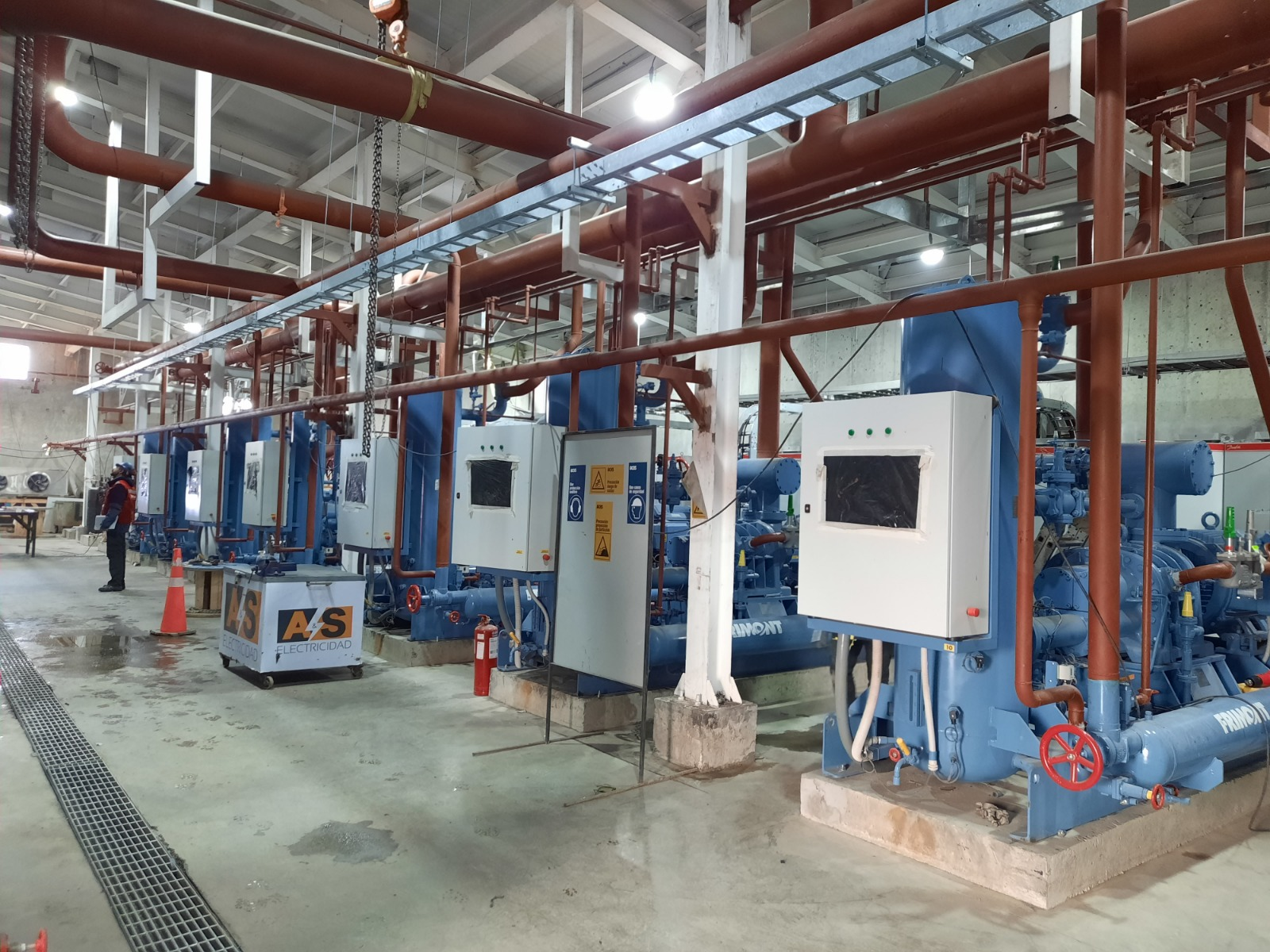 Sala de máquinas de refrigeración industrial con compresores azules, tableros eléctricos y cañerías.